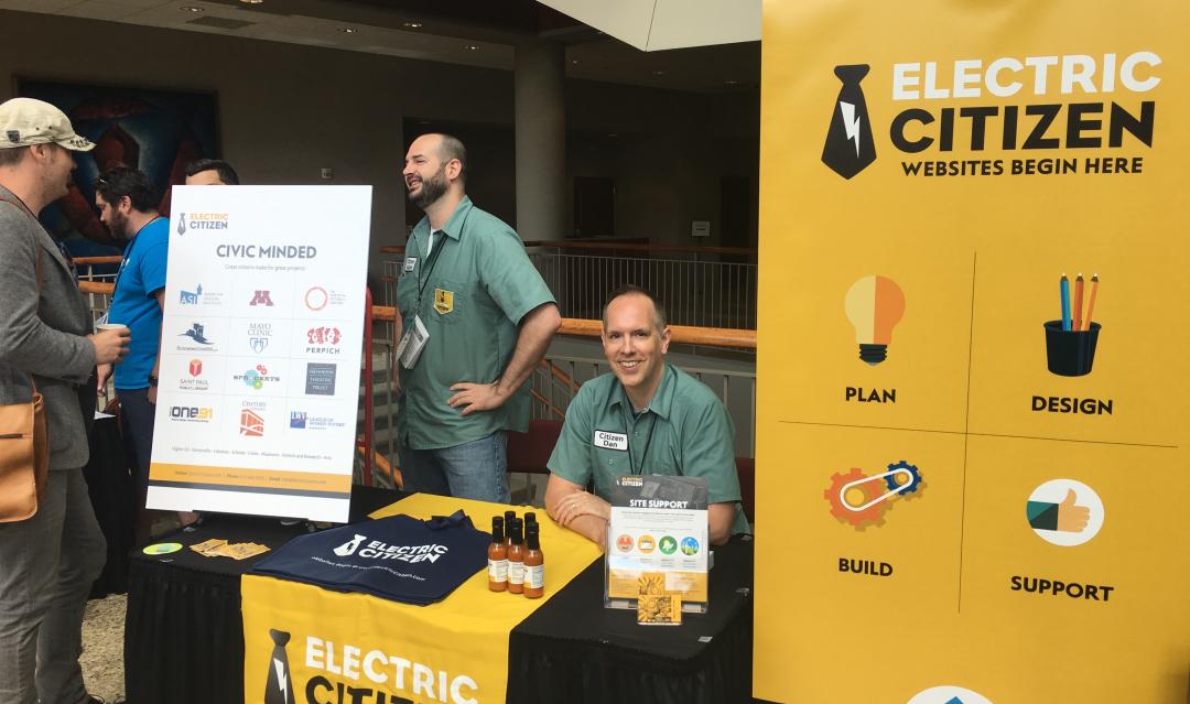 Dan and Adam talking to visitors at the Electric Citizen sponsor table with promotional signage