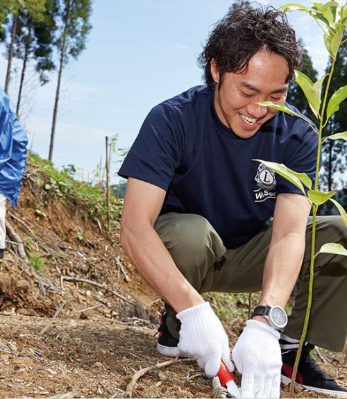 male volunteer helping others with planting, crouching in the dirt of a field