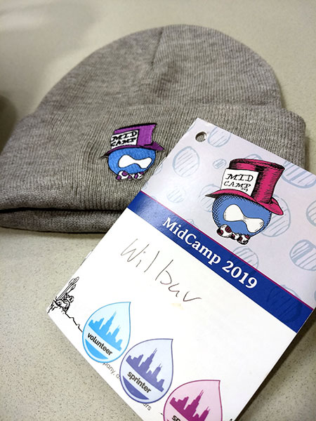 midcamp conference badge over a midcamp beanie hat