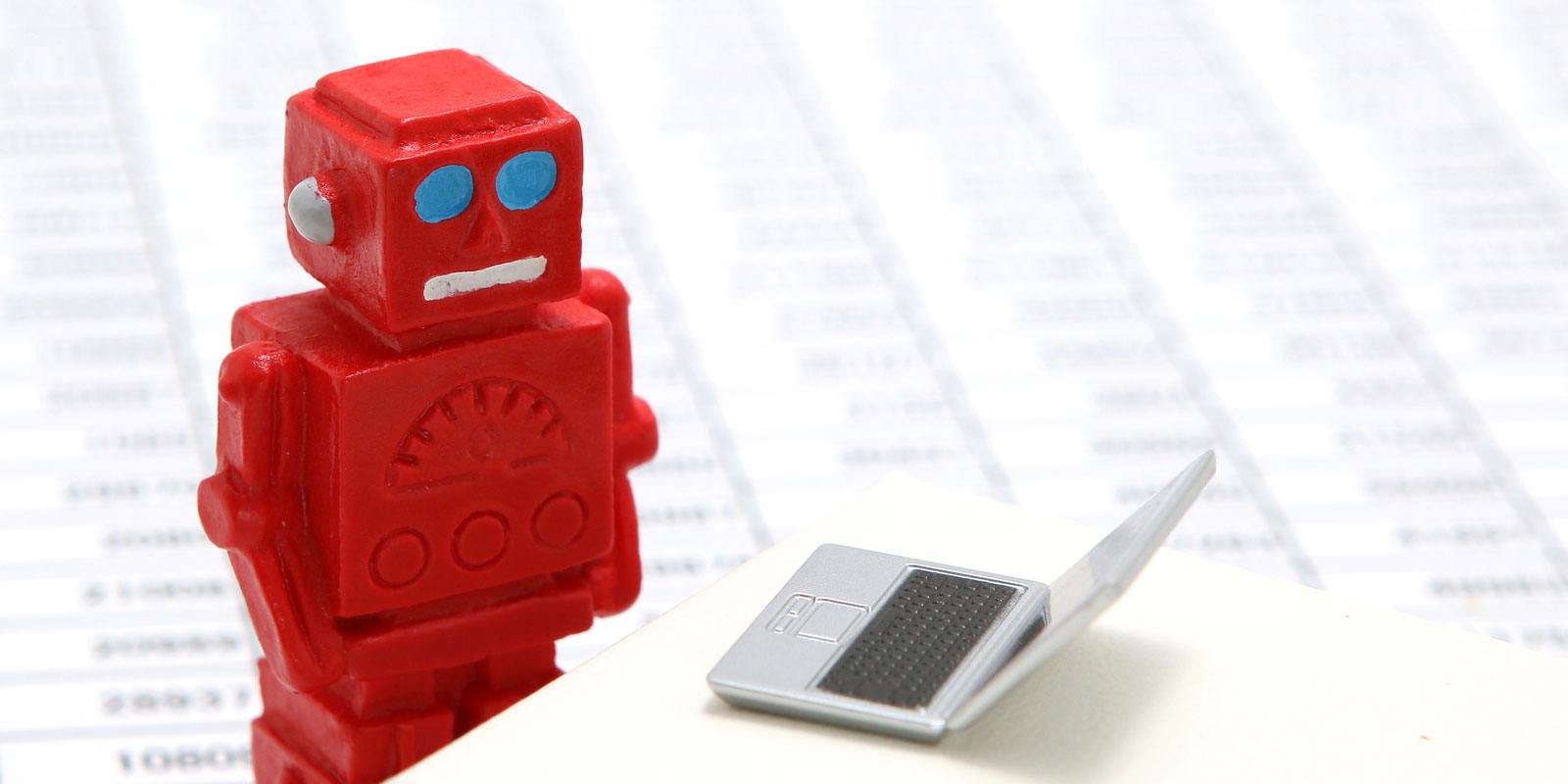 miniature red robot next to a tiny laptop