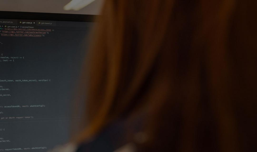 backside view of a person with long red hair looking at a computer screen and code