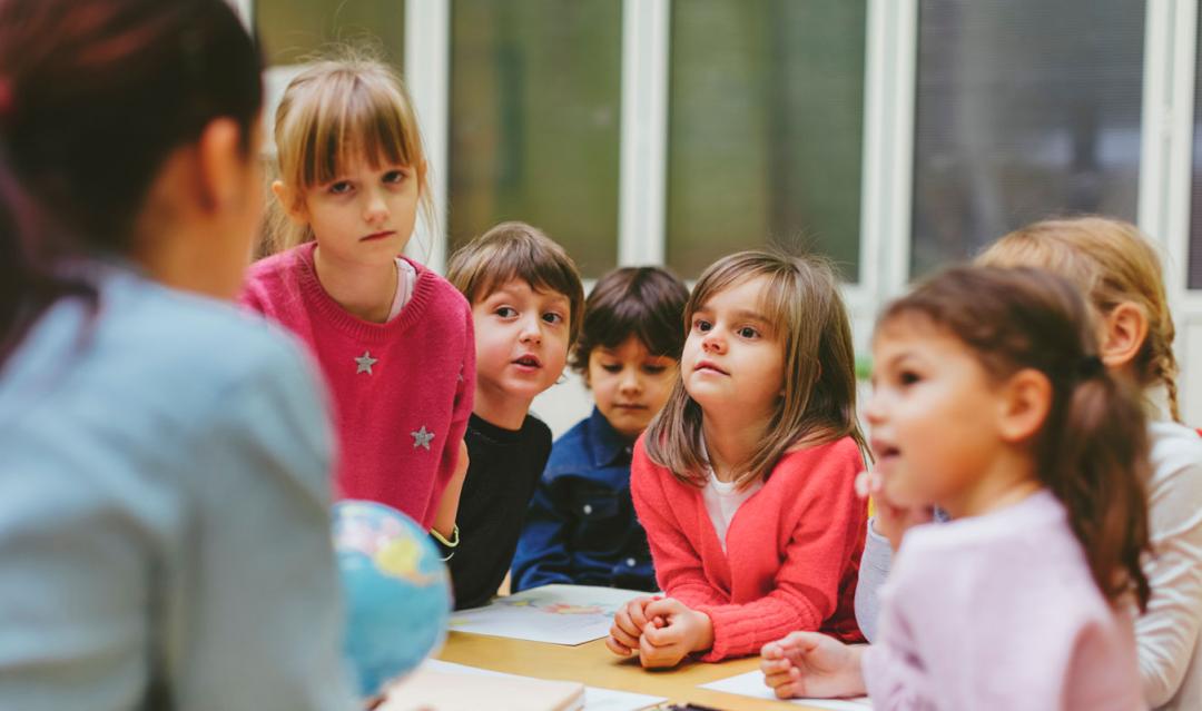 preschool children looking at their teacher, who is only seen from behind