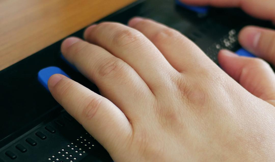 Close-up of a person's hands using computer with braille display