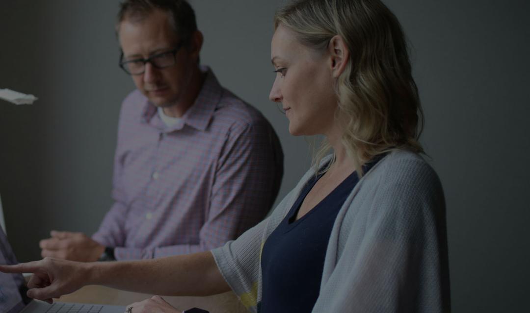 adult man and woman sharing a standing desk and reviewing a laptop together