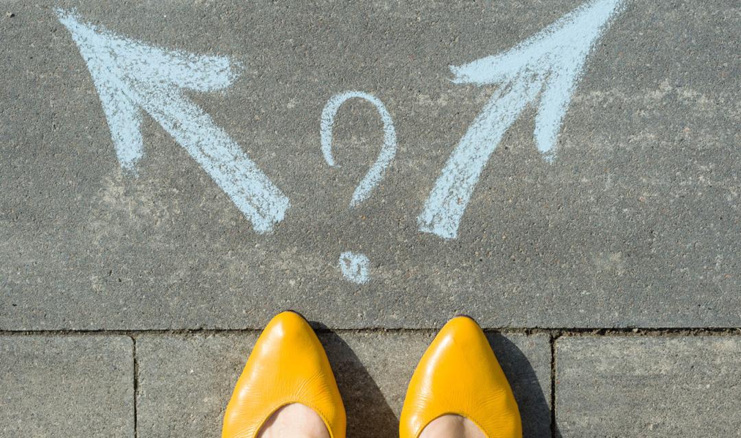 tips of gold shoes on woman's feet, standing before a sidewalk art of two arrows, a decision to be made