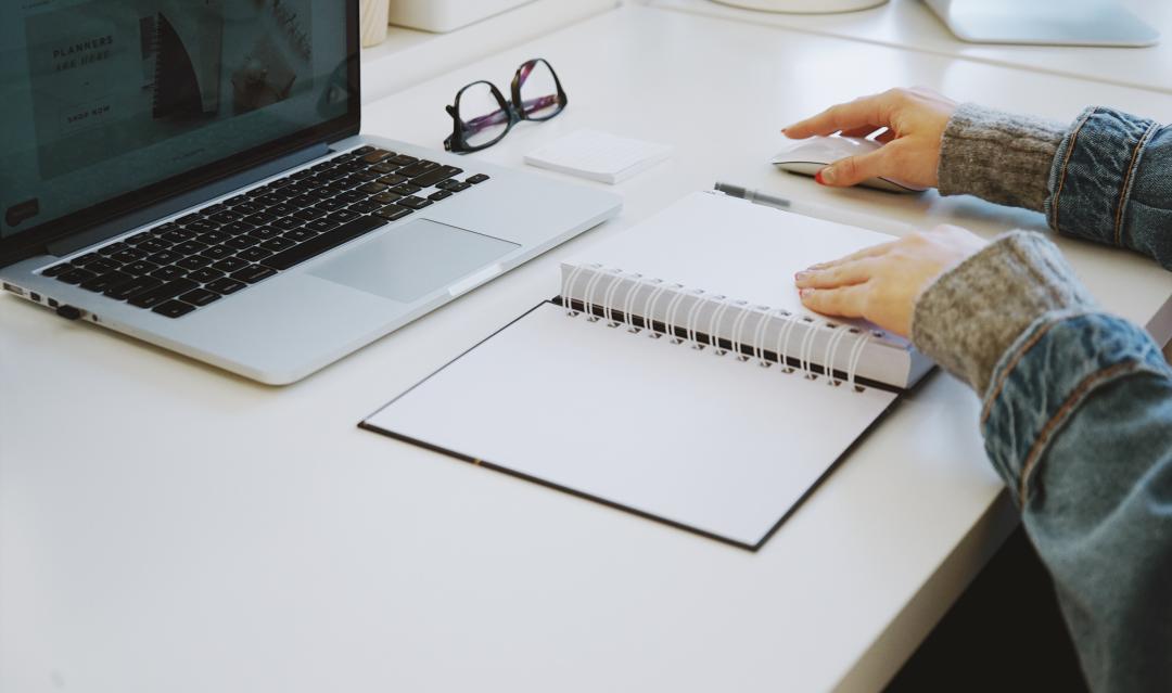 person writing in a notebook with computer nearby