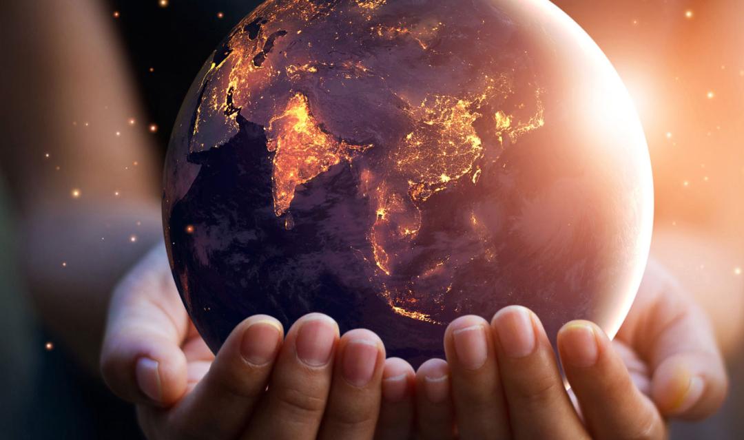 two hands holding a small, glowing globe against a dark background