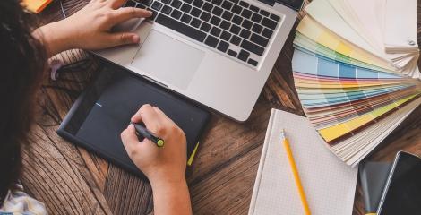 image of graphic designer working at desk, surrounded by laptop, color swatches, pen and paper