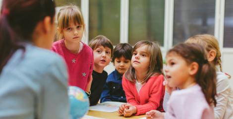 preschool children looking at their teacher, who is only seen from behind