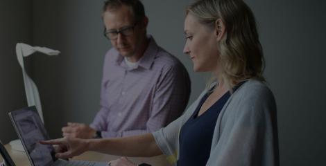 adult man and woman sharing a standing desk and reviewing a laptop together