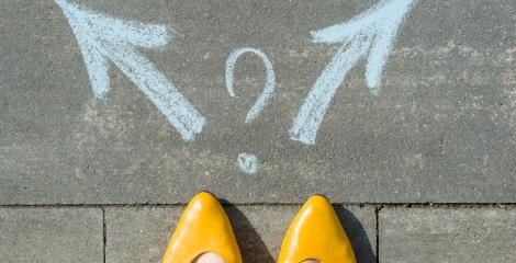 tips of gold shoes on woman's feet, standing before a sidewalk art of two arrows, a decision to be made