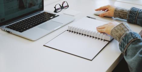 person writing in a notebook with computer nearby