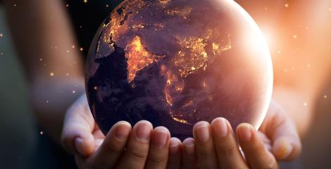 two hands holding a small, glowing globe against a dark background