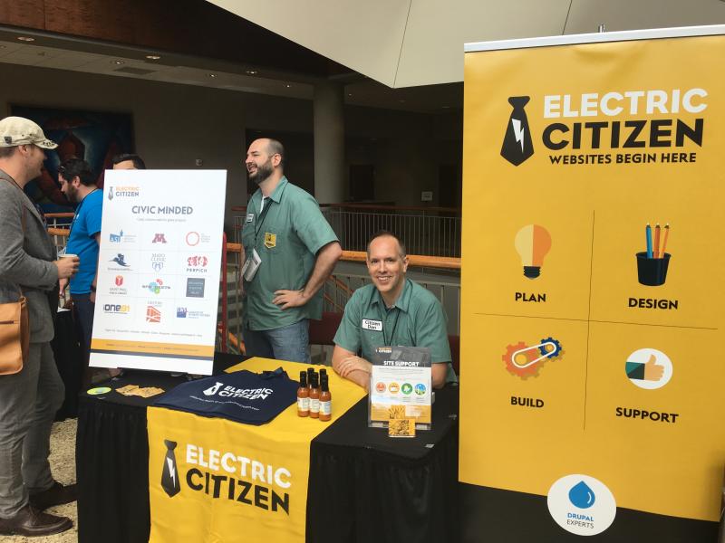 Dan and Adam talking to visitors at the Electric Citizen sponsor table with promotional signage