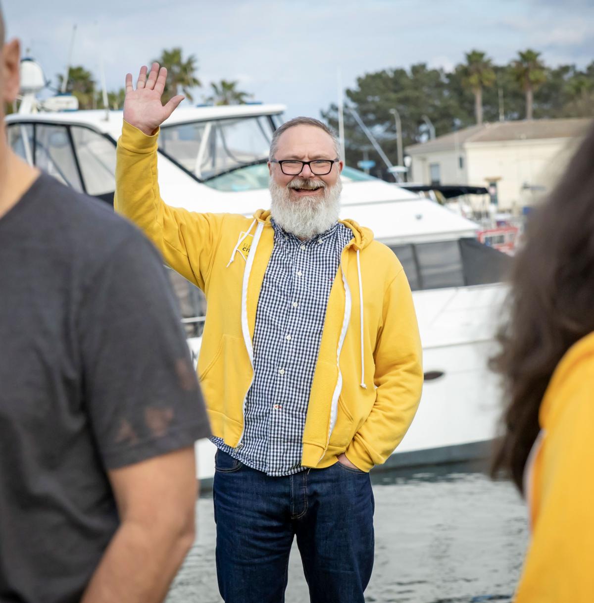 Brian waving to the camera with the bay and boats behind him