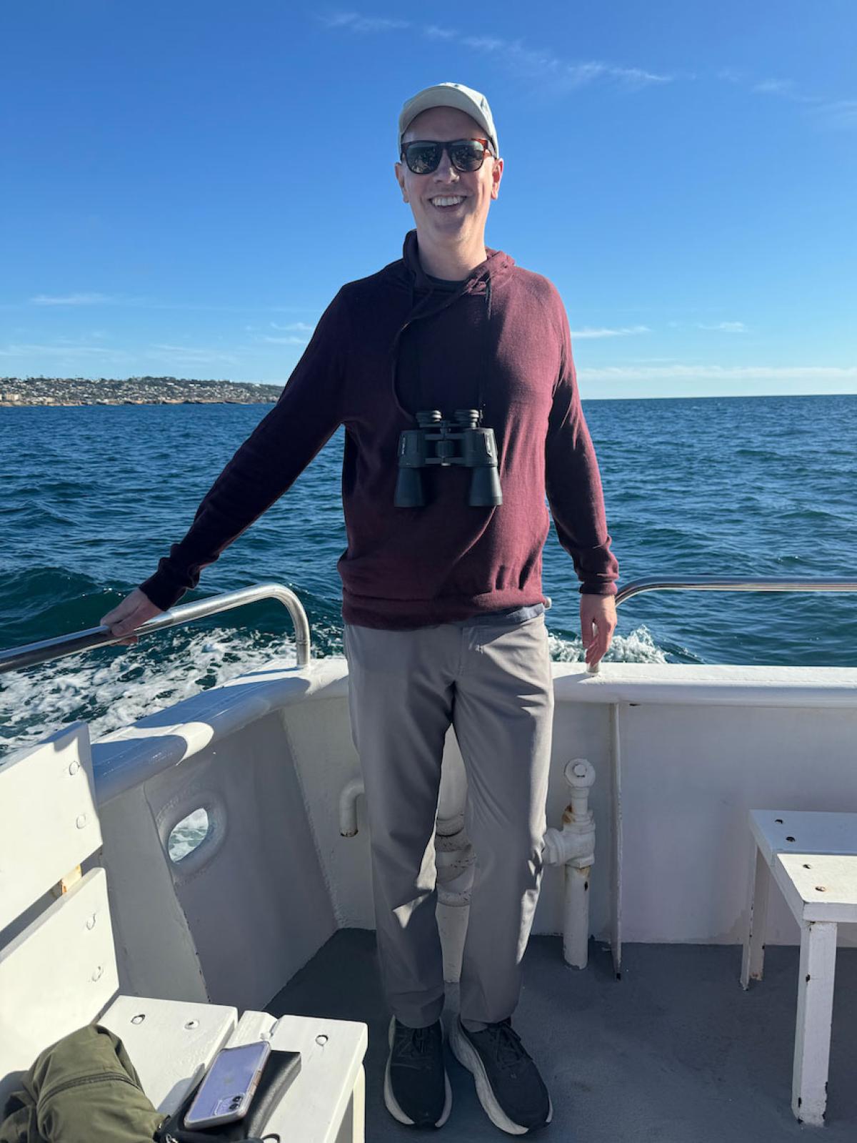 Dan on the boat wearing sunglasses and a dark red sweatshirt