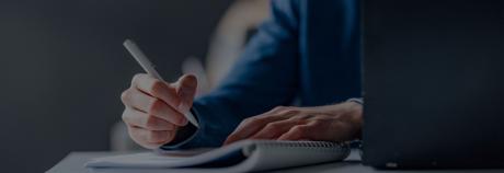 man taking notes with pen and paper, laptop is open