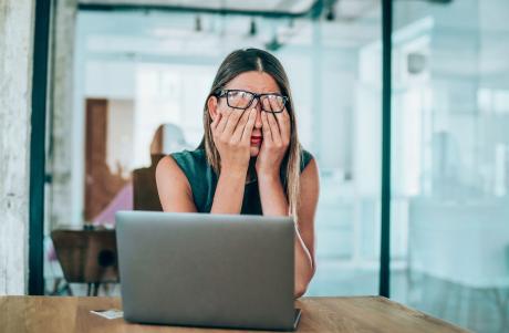 frustrated and confused woman sitting in an office in front of her laptop, covering her eyes