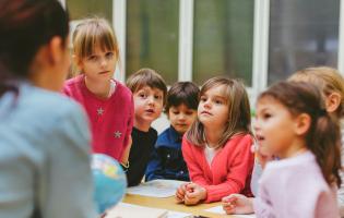 preschool children looking at their teacher, who is only seen from behind