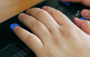 Close-up of a person's hands using computer with braille display