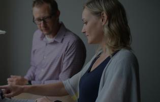 adult man and woman sharing a standing desk and reviewing a laptop together