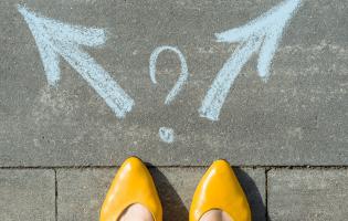 tips of gold shoes on woman's feet, standing before a sidewalk art of two arrows, a decision to be made