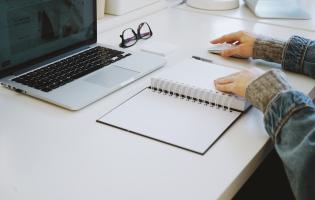 person writing in a notebook with computer nearby