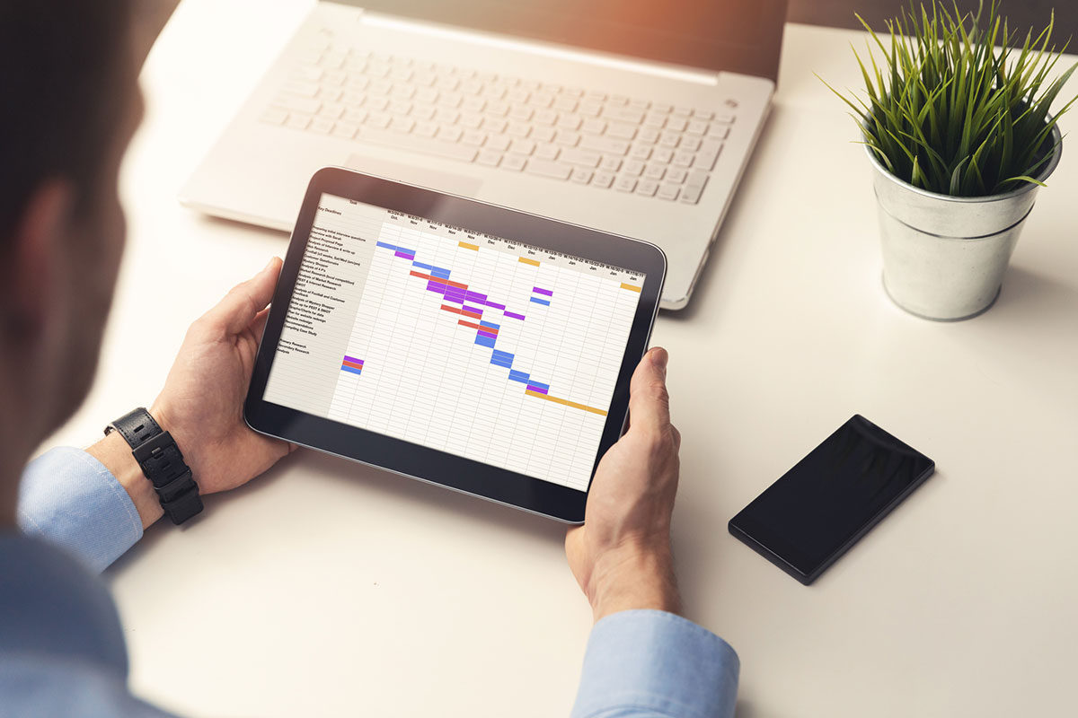 hands of person at work with a computer tablet displaying a gantt chart timeline