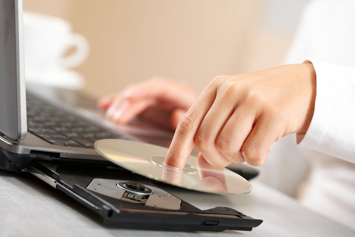 hands of person at work, placing a CD in a laptop tray for reading